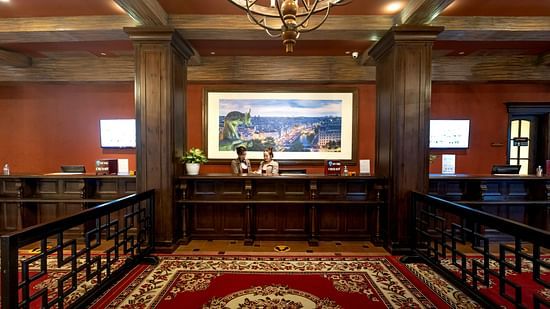 a carpeted front desk lobby with cosy interiors and two staff members standing behind the desk